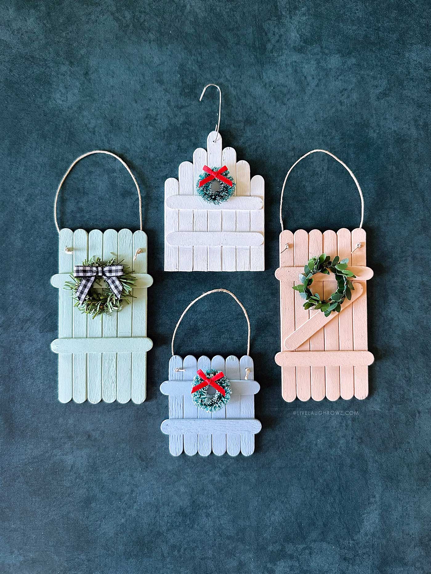 Four finished popsicle stick ornaments in pastel colors decorated with wreaths and bows.