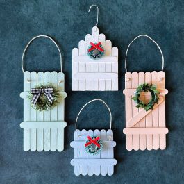 Four finished popsicle stick fence ornaments in pastel colors decorated with wreaths and bows.