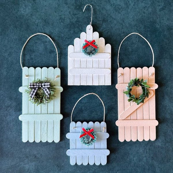 Four finished popsicle stick fence ornaments in pastel colors decorated with wreaths and bows.