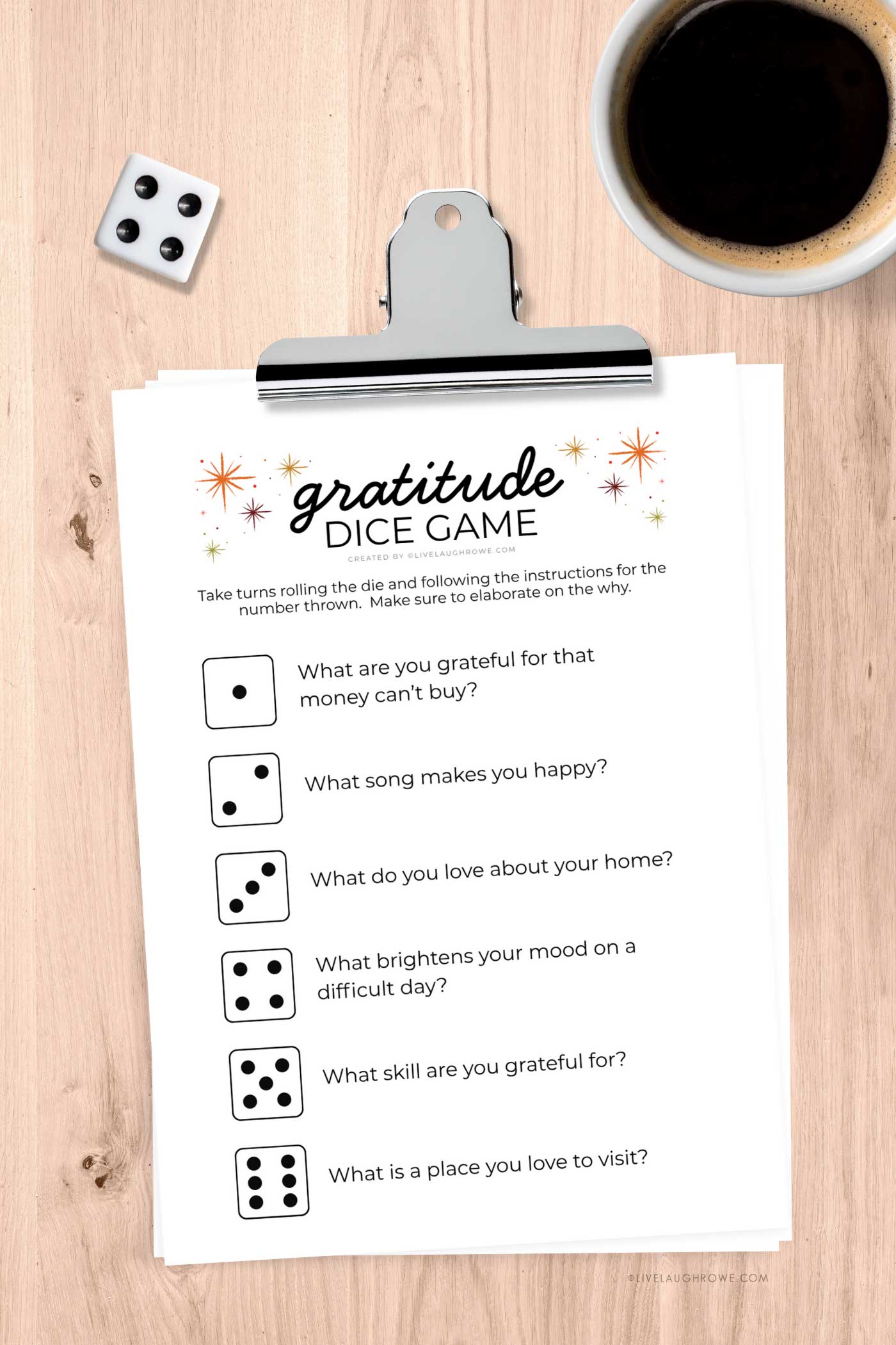 Clipboard displaying the Gratitude Dice Game printable alongside a die and a coffee cup, ready for play.