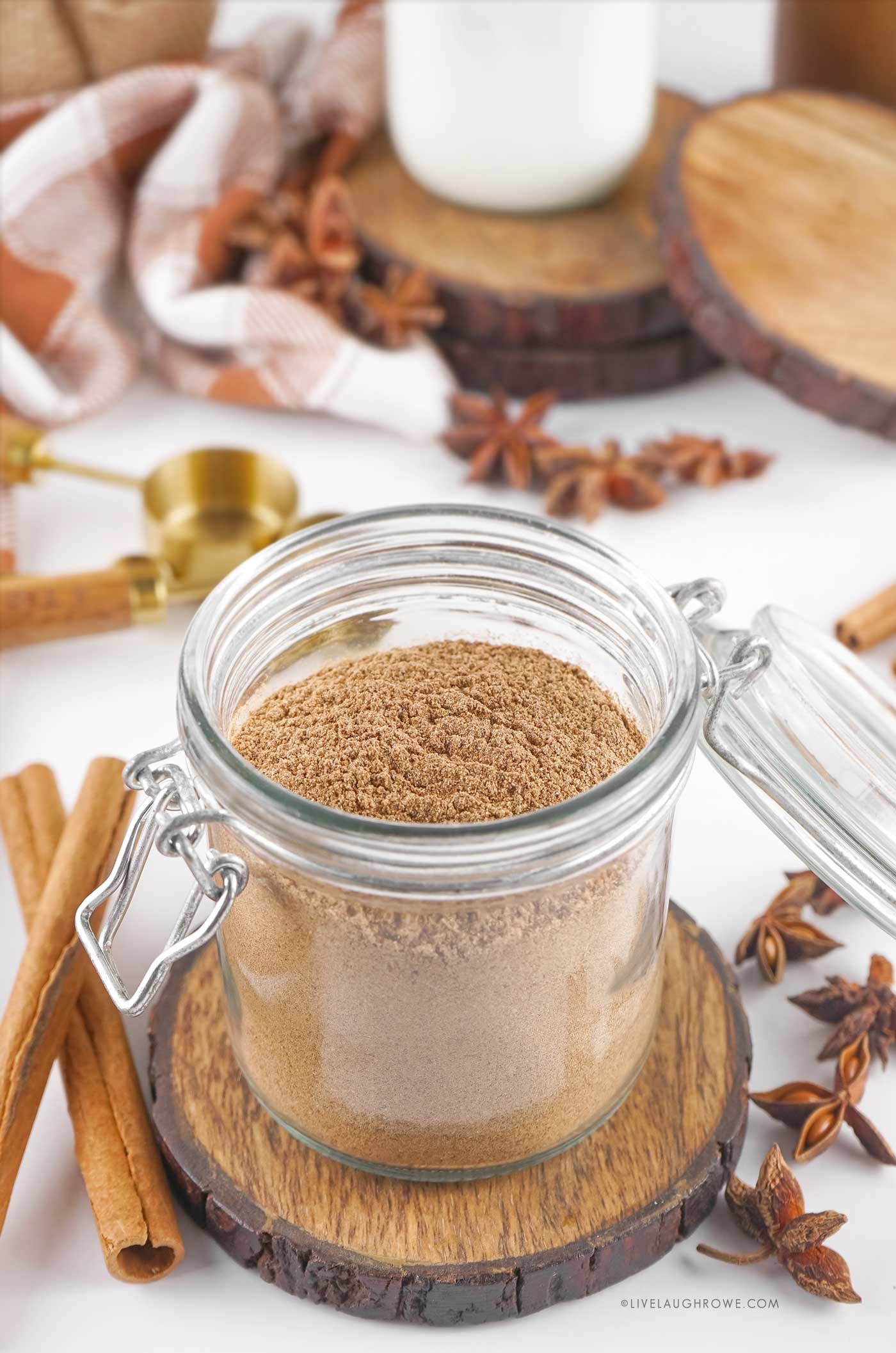 A glass jar filled with aromatic chai spice sitting on a wooden counter with a spoon beside it — warm, rustic, and ready for gifting.