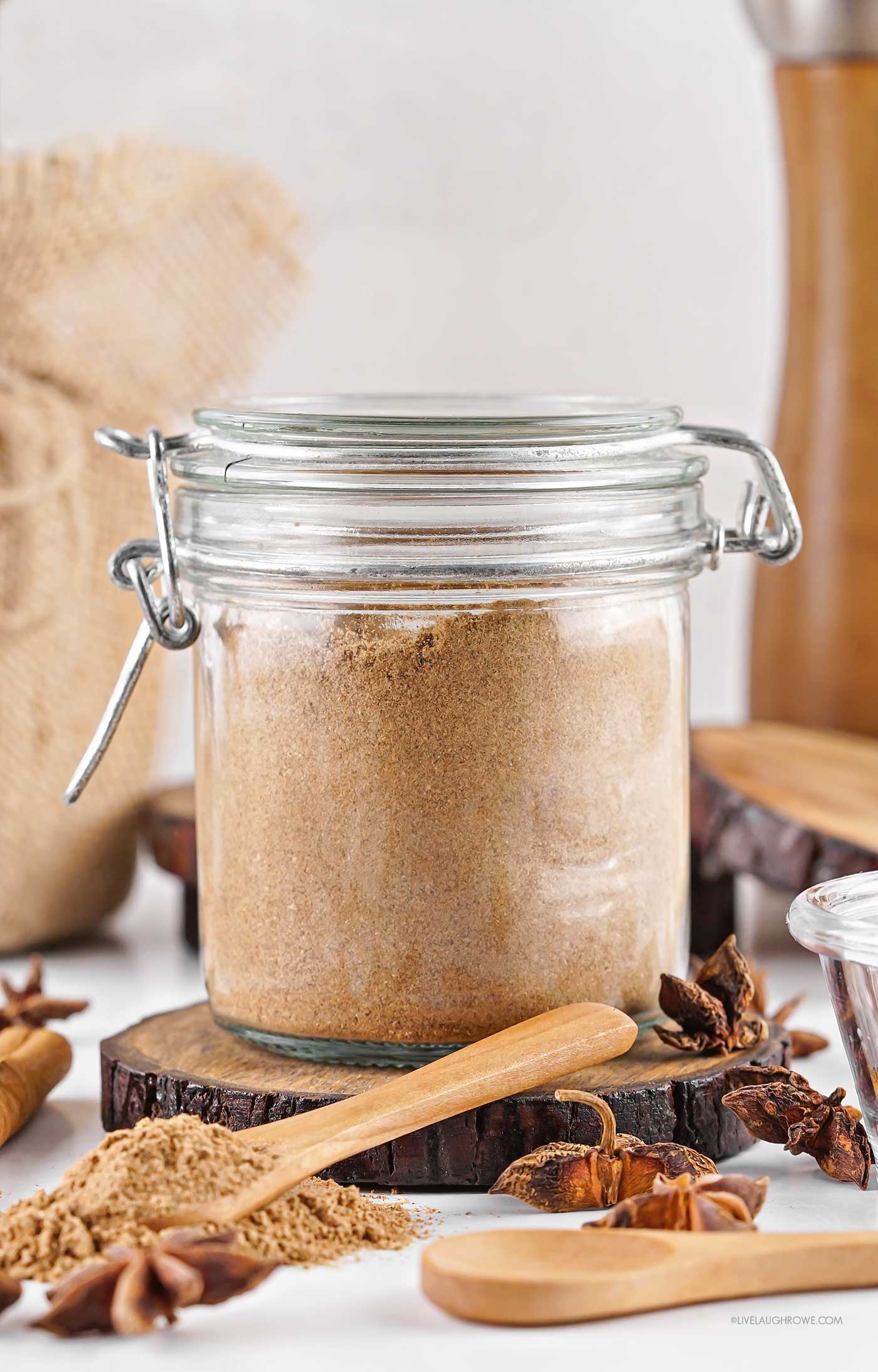 A glass jar filled with aromatic chai spice sitting on a wooden counter with a spoon beside it — warm, rustic, and ready for gifting.