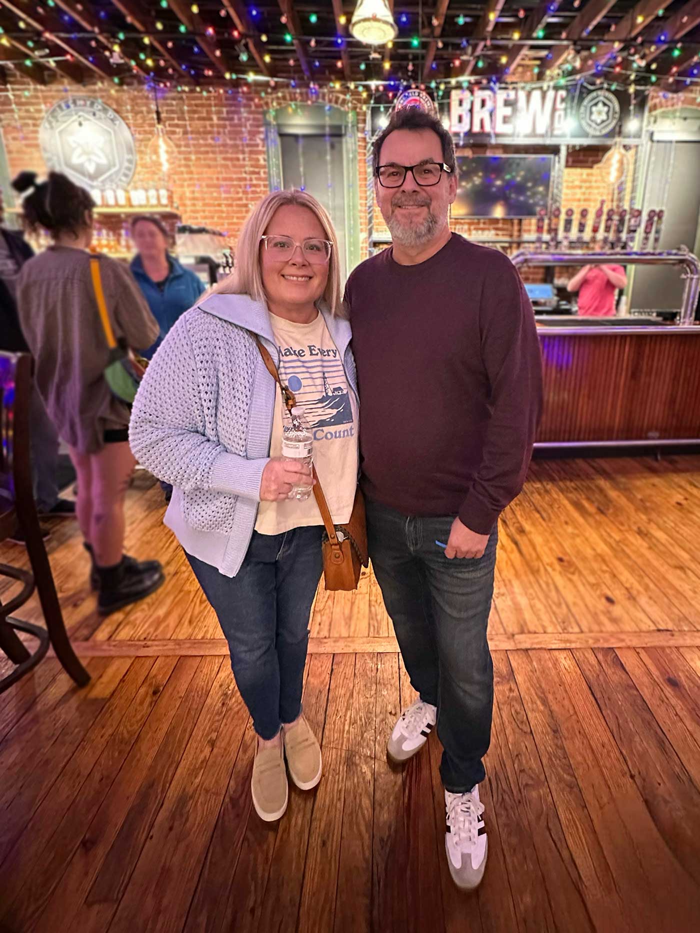 Smiling couple at a local brewery with string lights and a cozy atmosphere.