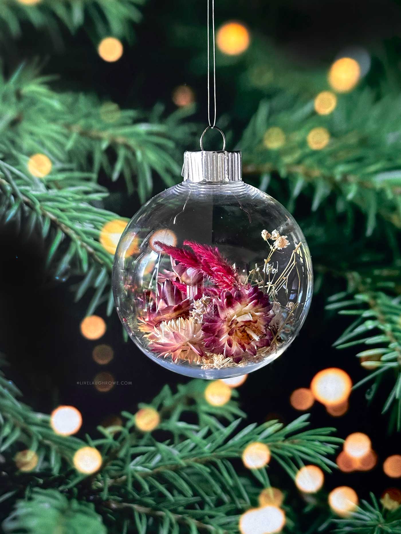 Hanging Dried Flower Ornament against evergreen branches and warm holiday lights.