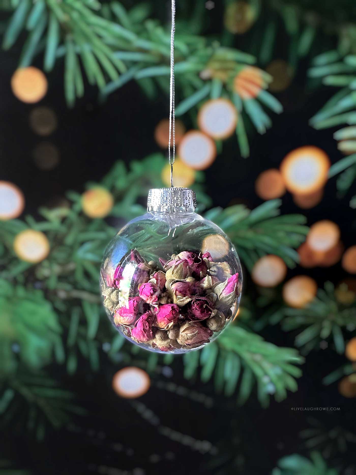 Hanging ornament filled with rosebuds against evergreen branches and warm holiday lights.