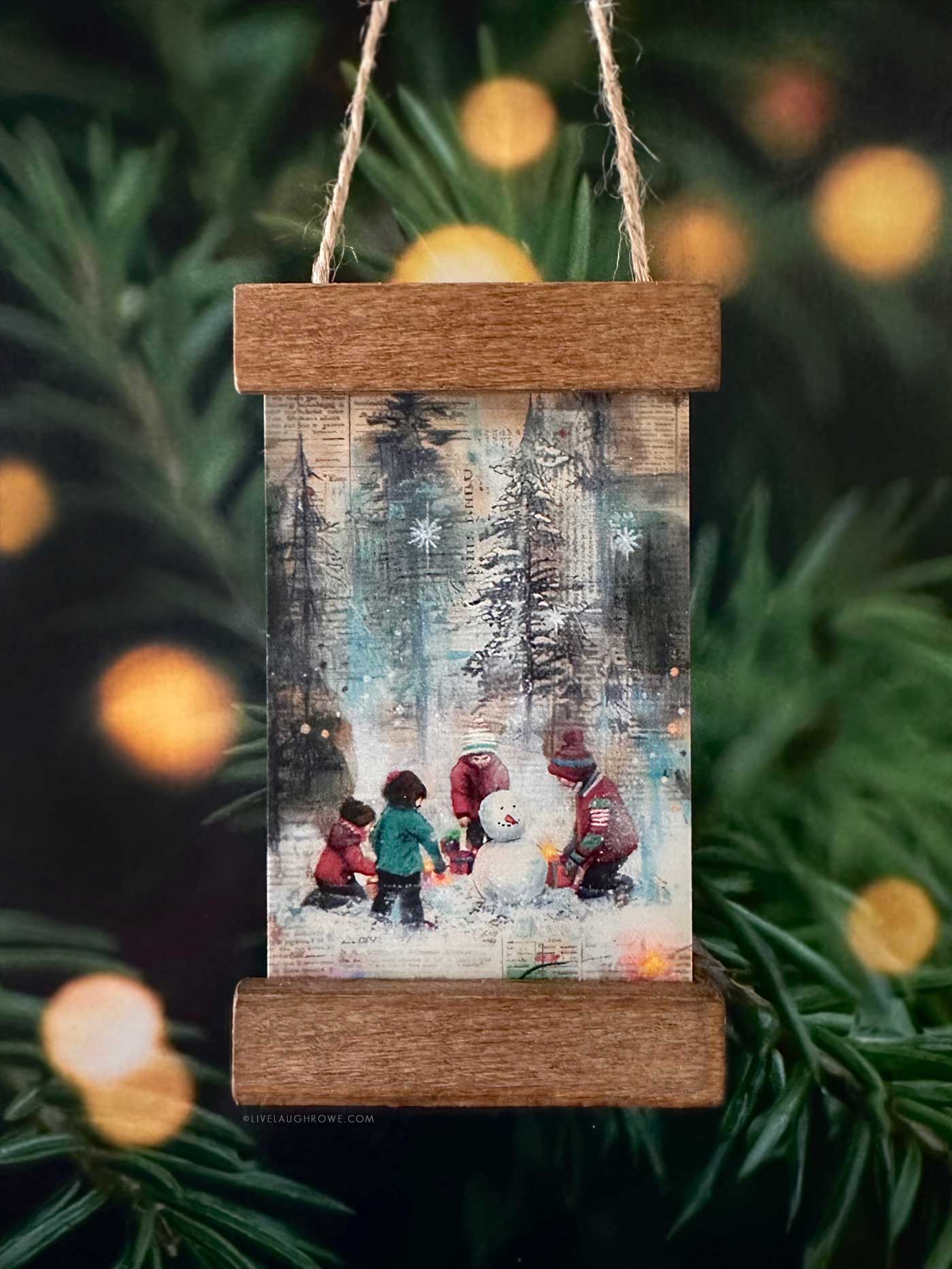 Handmade Christmas ornament featuring a winter scene print of children building a snowman in a mini poster hanger ornament.