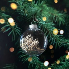Finished ornament filled with dried baby’s breath hanging on a Christmas tree with warm glowing lights.