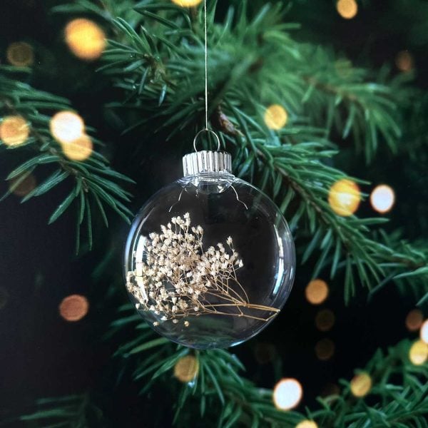 Finished ornament filled with dried baby’s breath hanging on a Christmas tree with warm glowing lights.
