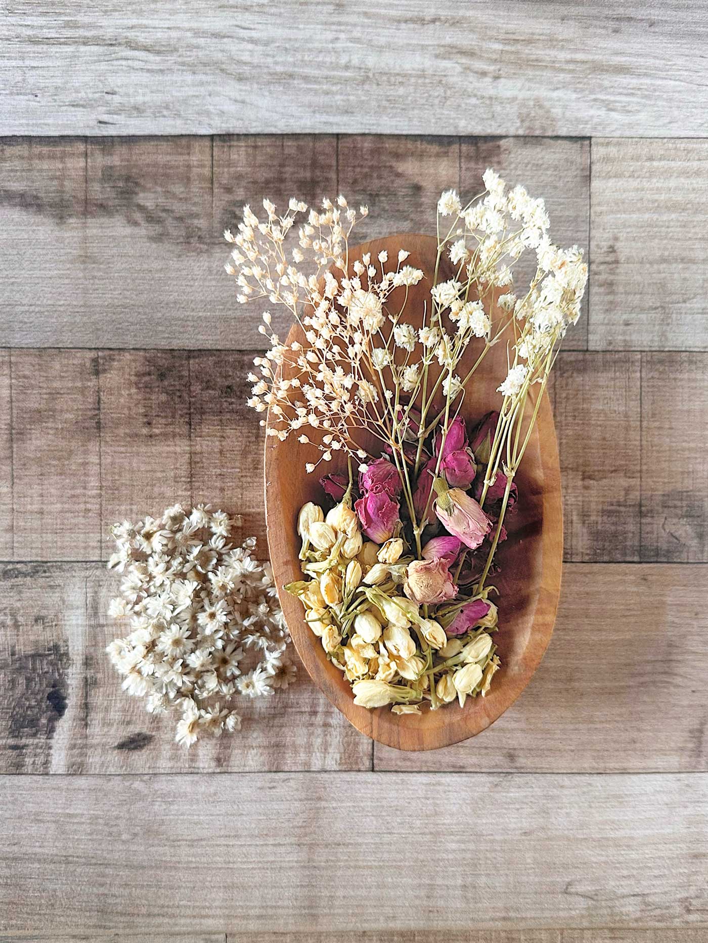 Supplies for making dried flower ornaments, including dried jasmine, mini star flowers, baby’s breath, and rosebuds arranged in a wooden bowl.