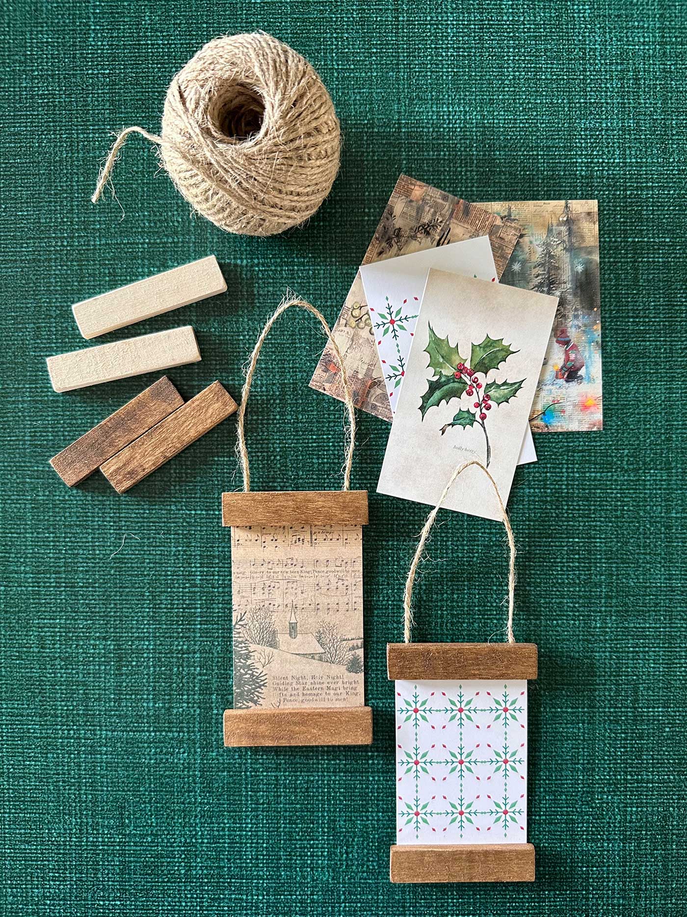 Several mini poster hanger ornaments being assembled, featuring holly artwork and rustic stained wood.