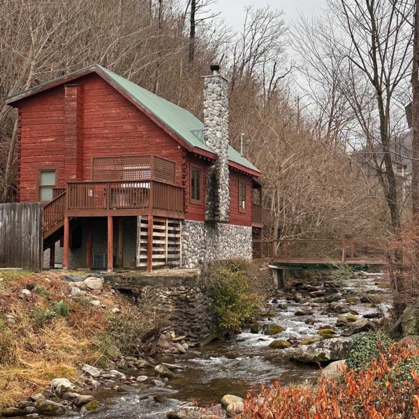 Rustic red cabin perched beside a flowing creek in Gatlinburg, Tennessee, surrounded by winter trees