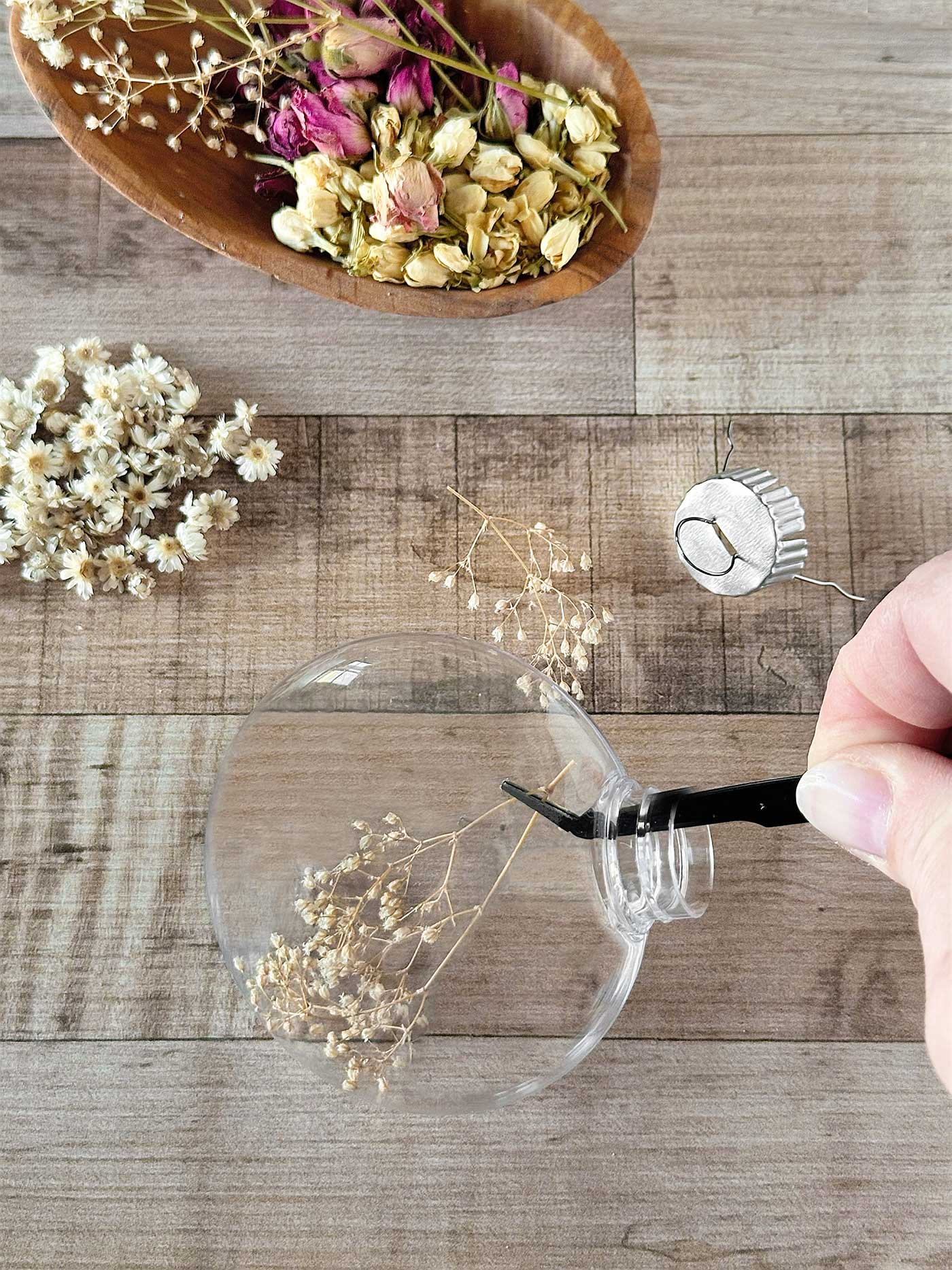 Hand placing baby’s breath into a clear ornament while assembling DIY dried flower ornaments.