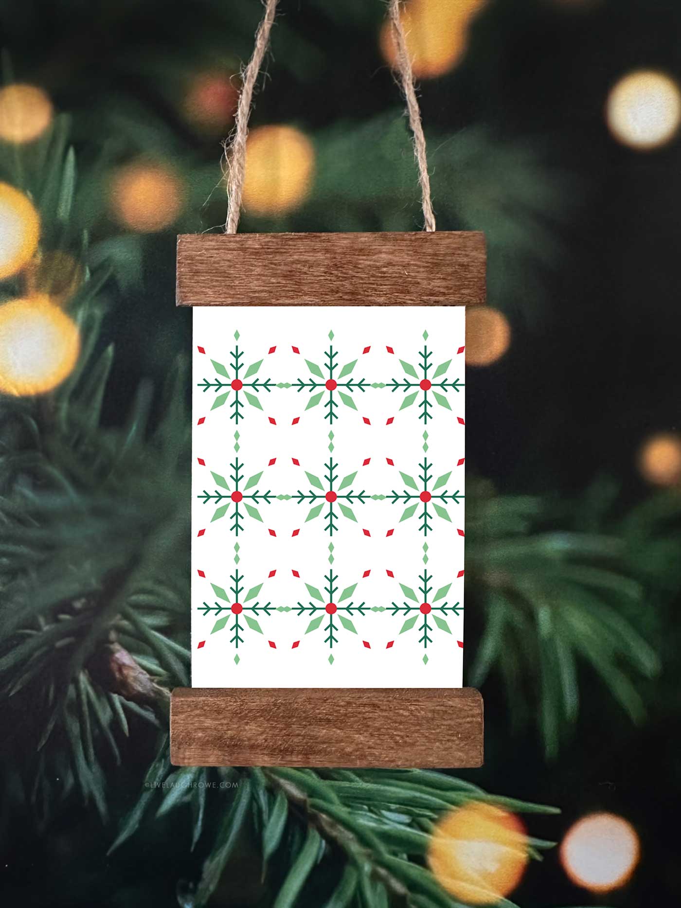 Handmade Christmas ornament featuring a green and red patterned print displayed in a mini poster hanger ornament with wooden strips and twine.