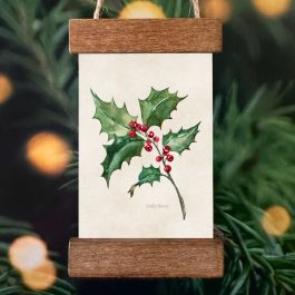 Festive ornament featuring a holly illustration displayed in a mini poster hanger ornament hanging on a Christmas tree.