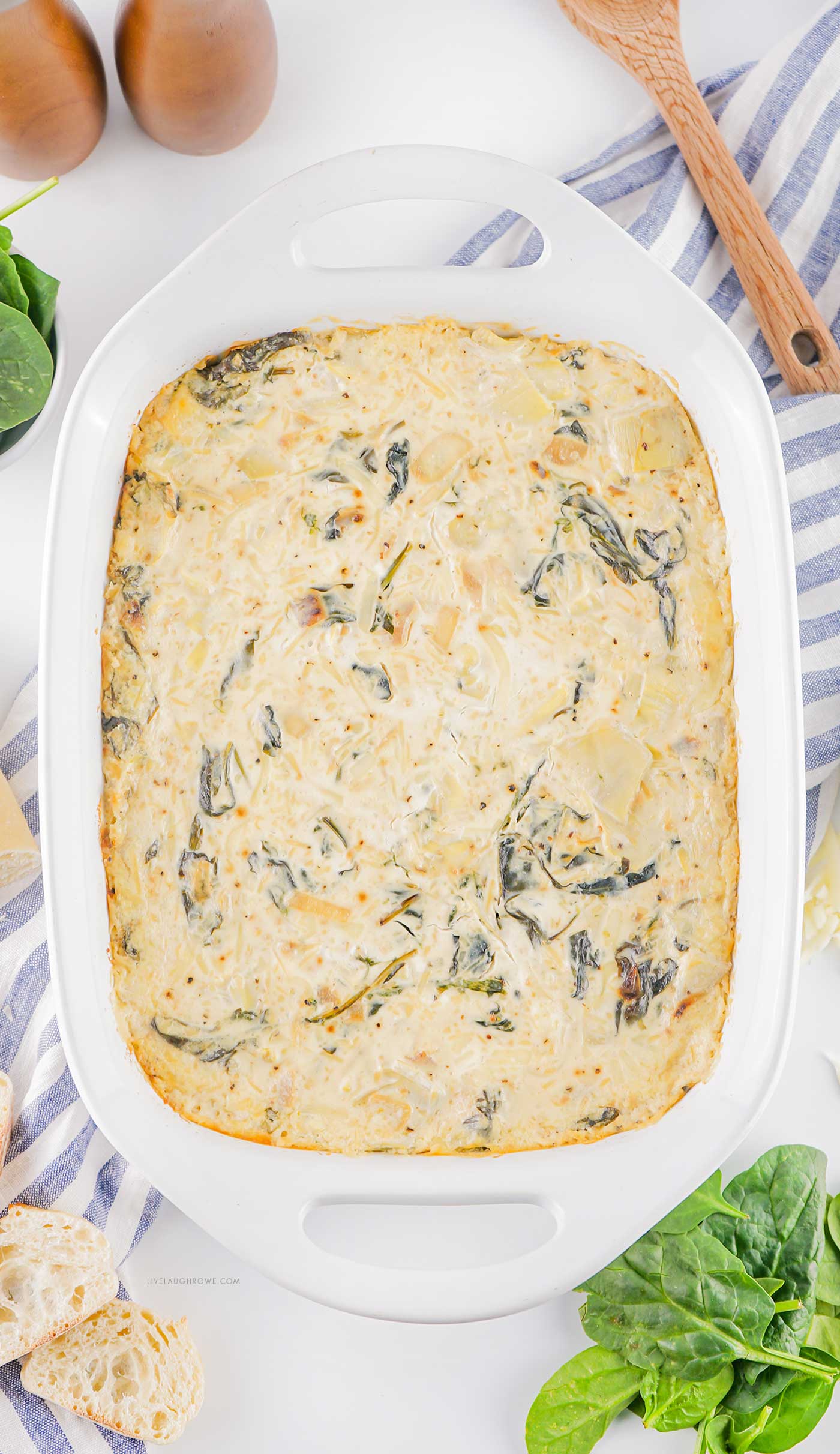 Overhead view of baked spinach artichoke dip in a white baking dish, golden and creamy.