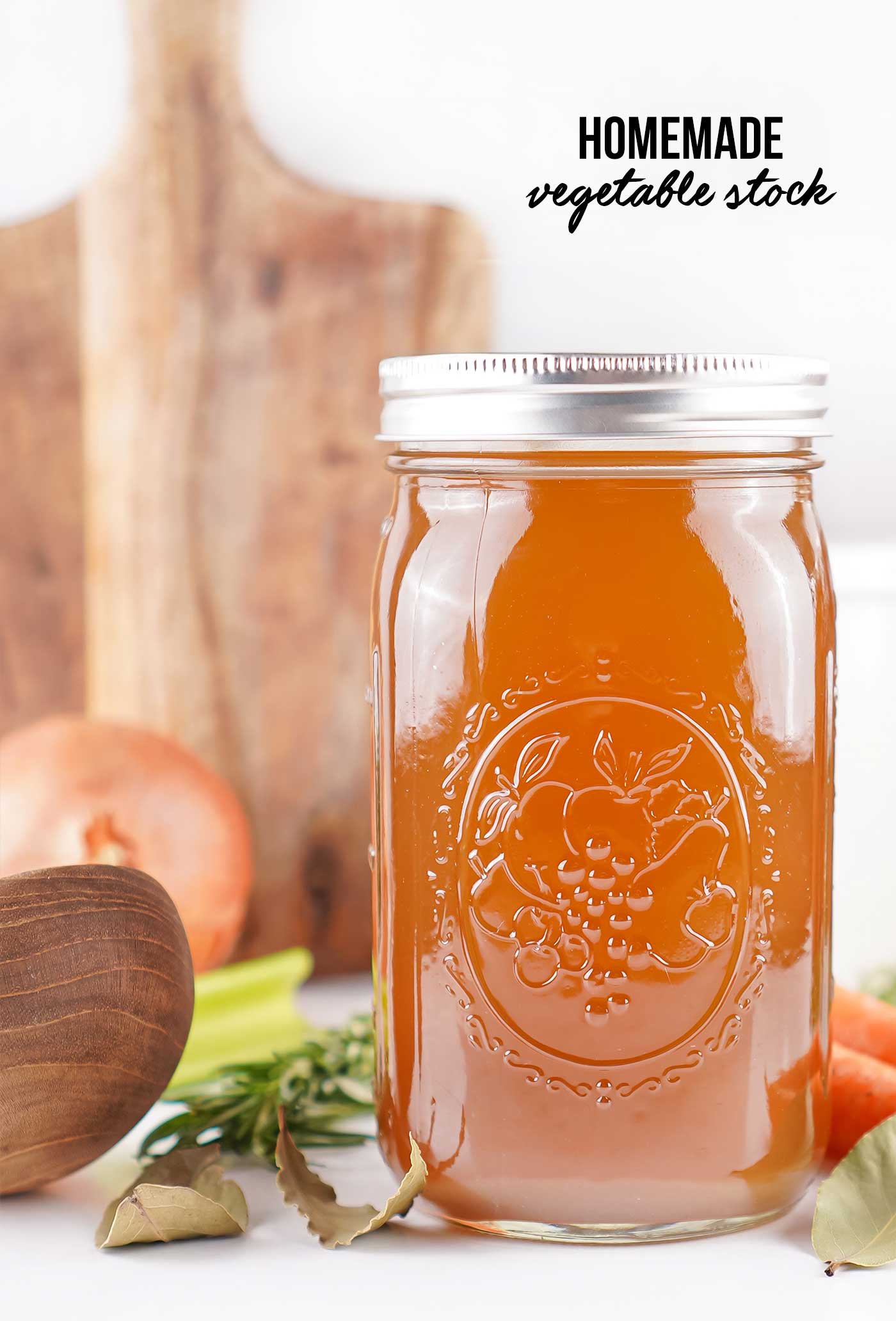 Tall mason jar of homemade soup stock with fresh vegetables and herbs styled on a rustic wooden background.