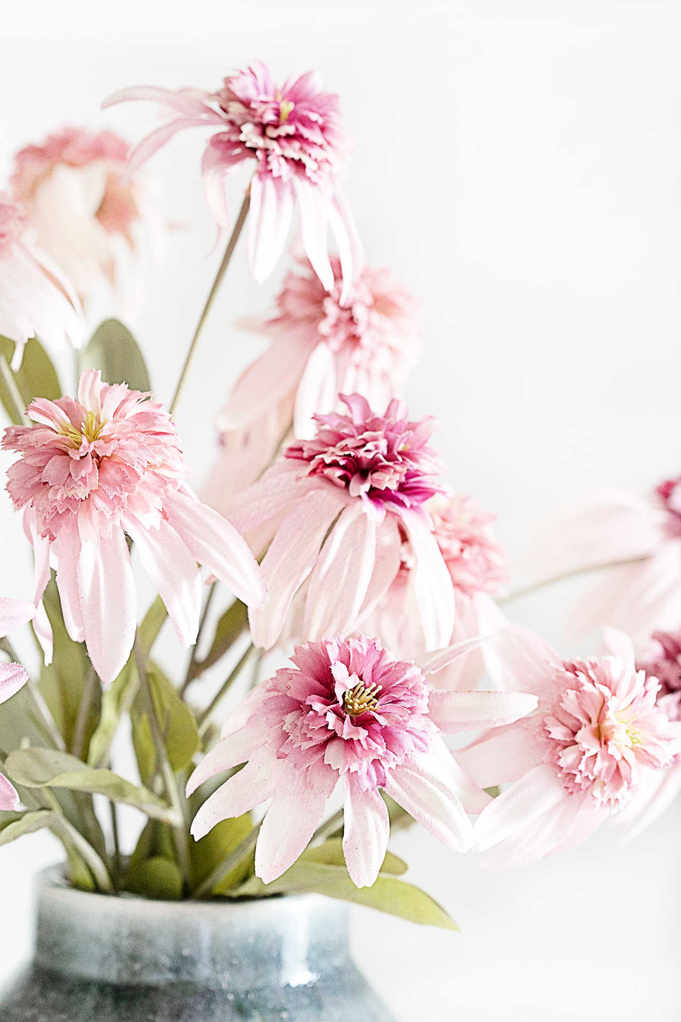 Soft pink faux spring flowers with layered petals arranged in a vase against a light, airy background.