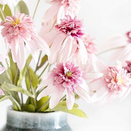 Soft pink faux spring flowers with layered petals arranged in a vase against a light, airy background.