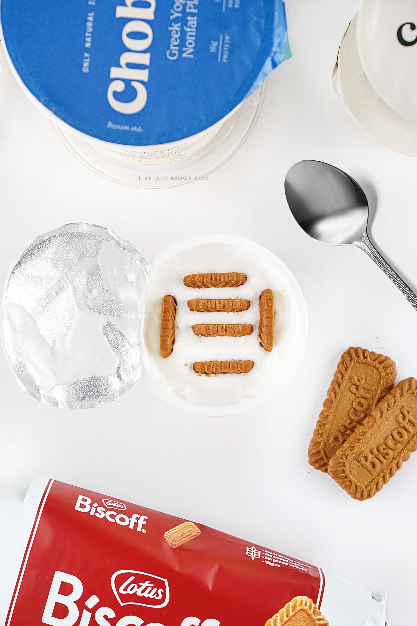 Ingredients for viral Japanese cheesecake including Greek yogurt cups and Biscoff cookies arranged on a white background.