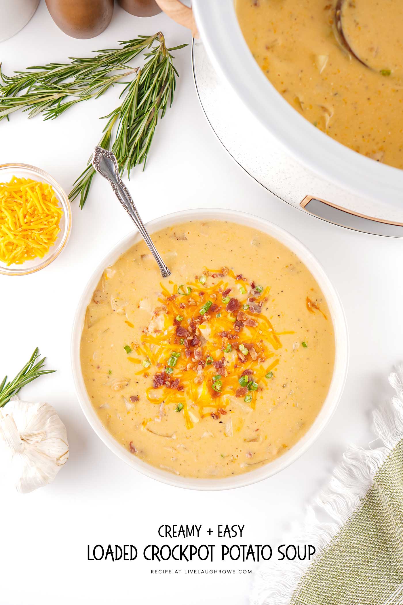 Overhead view of loaded crockpot crack potato soup served in a white bowl with melted cheddar, crispy bacon, and green onions.