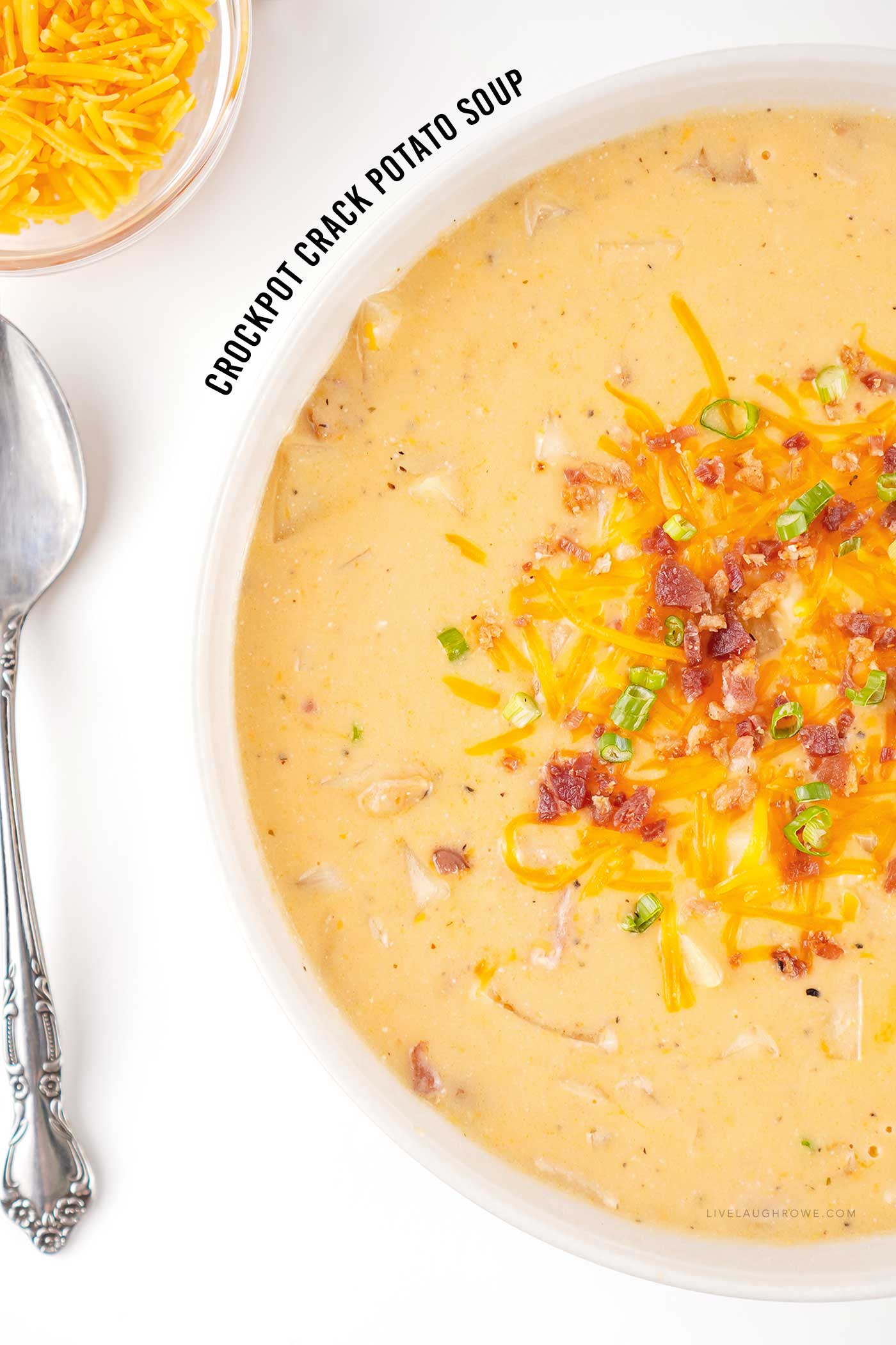 Close up of crockpot crack potato soup topped with shredded cheddar cheese, crispy bacon, and chopped green onions.