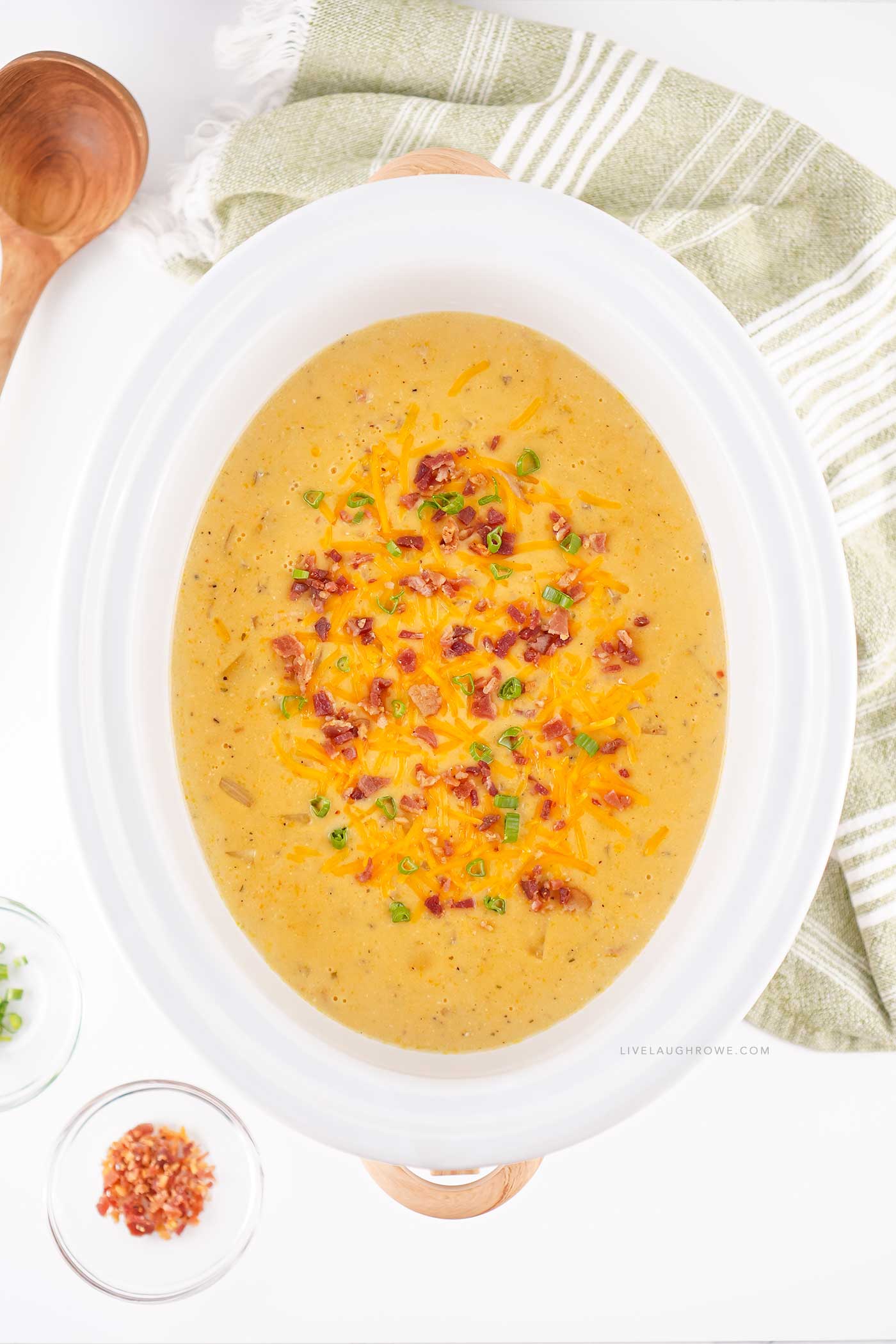slow cooker of rich potato soup garnished with green onions and crispy bacon.