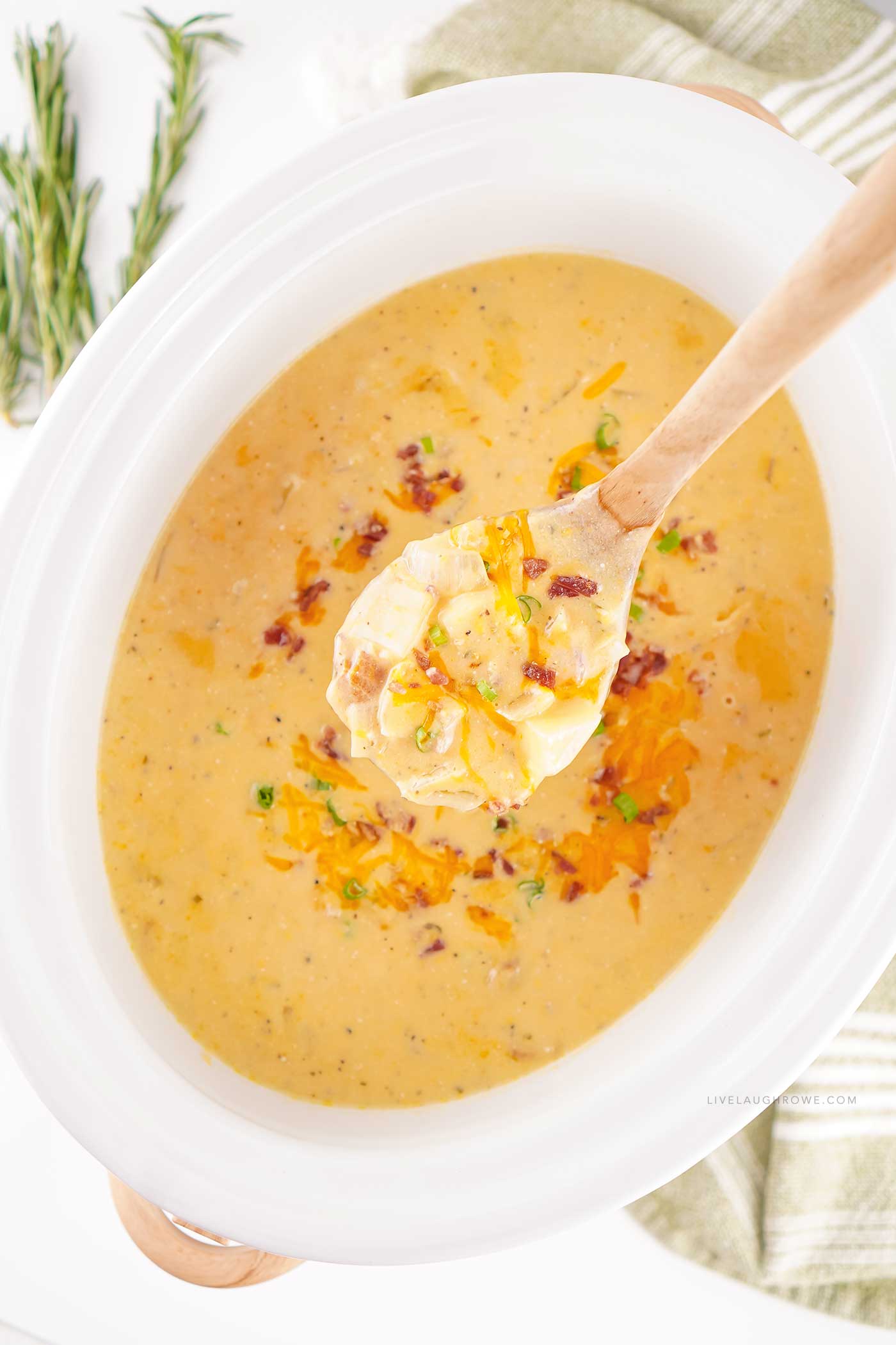 Spoon lifting creamy potato soup from a white slow cooker.