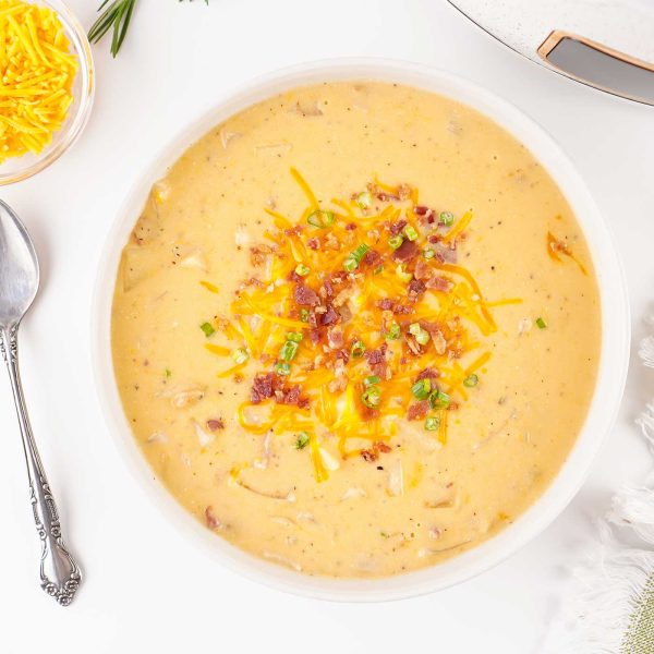 Creamy slow cooker loaded potato soup served in a white bowl with shredded cheddar and crumbled bacon as garnish.