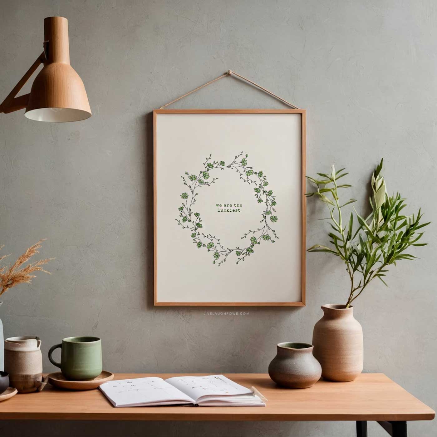 Framed &ldquo;We Are the Luckiest&rdquo; wall art printable with botanical wreath displayed on a table with greenery