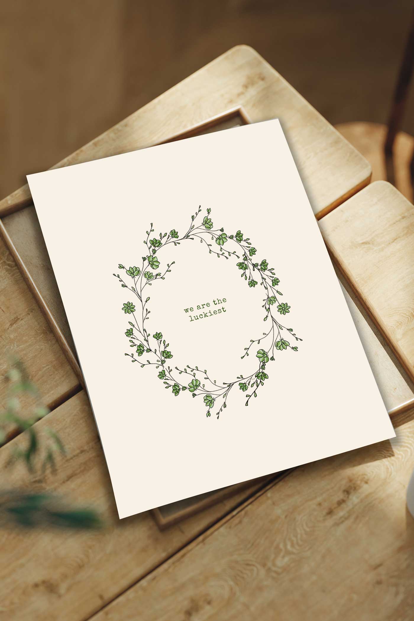 &ldquo;We Are the Luckiest&rdquo; wall art printable with botanical wreath on a wooden table