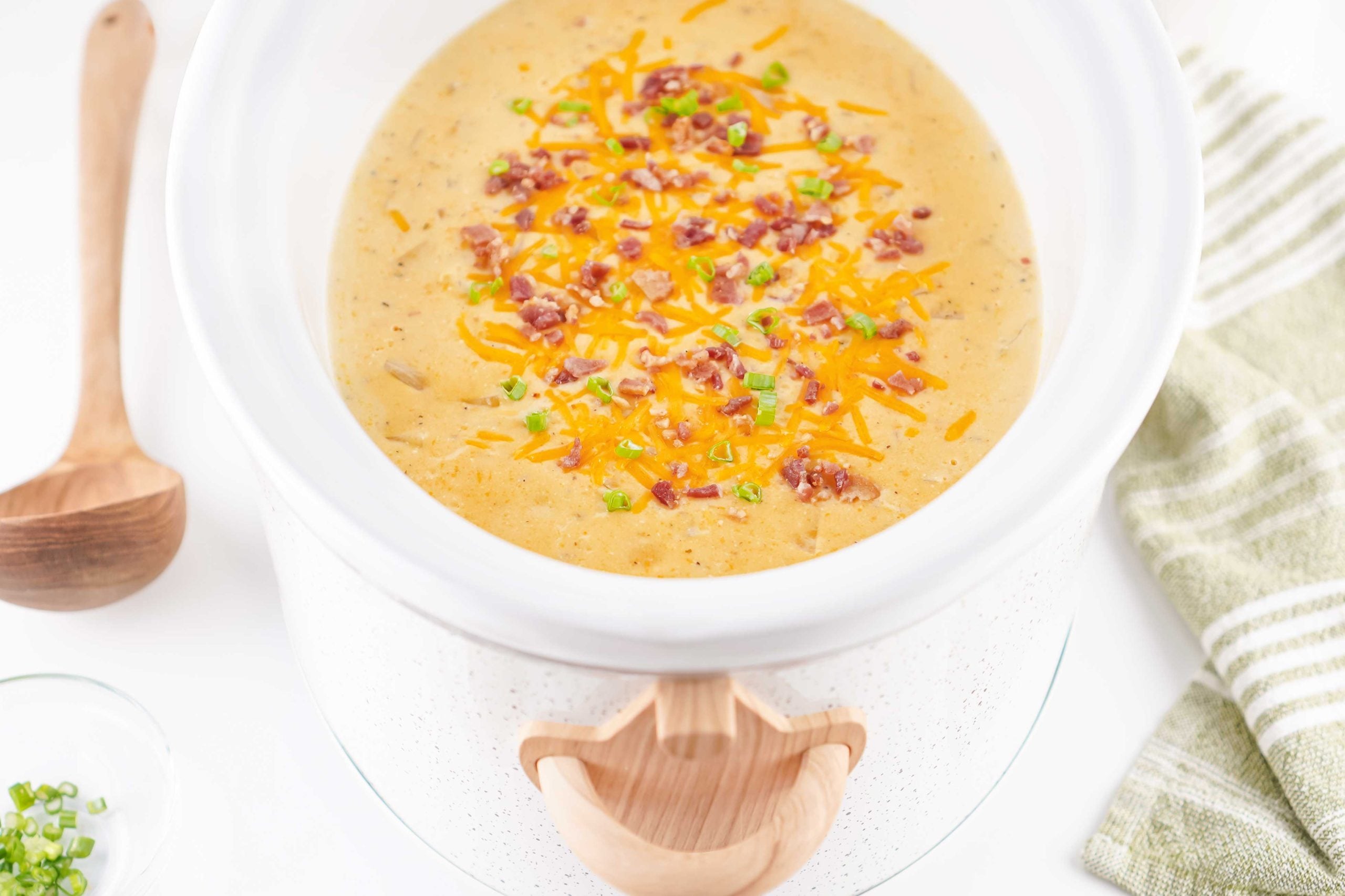 easy crockpot crack potato soup topped with cheddar cheese, bacon, and green onions in a white slow cooker