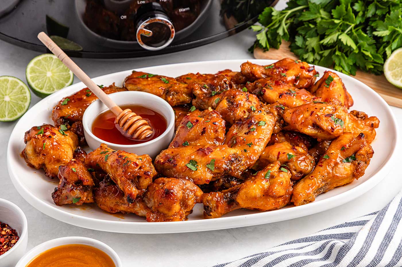 hot honey chicken wings served on a platter with honey dipping sauce and lime wedges
