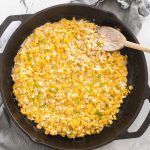 Close-up of honey butter skillet corn being stirred in a cast iron skillet with a wooden spoon