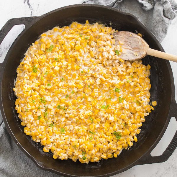 Close-up of honey butter skillet corn being stirred in a cast iron skillet with a wooden spoon