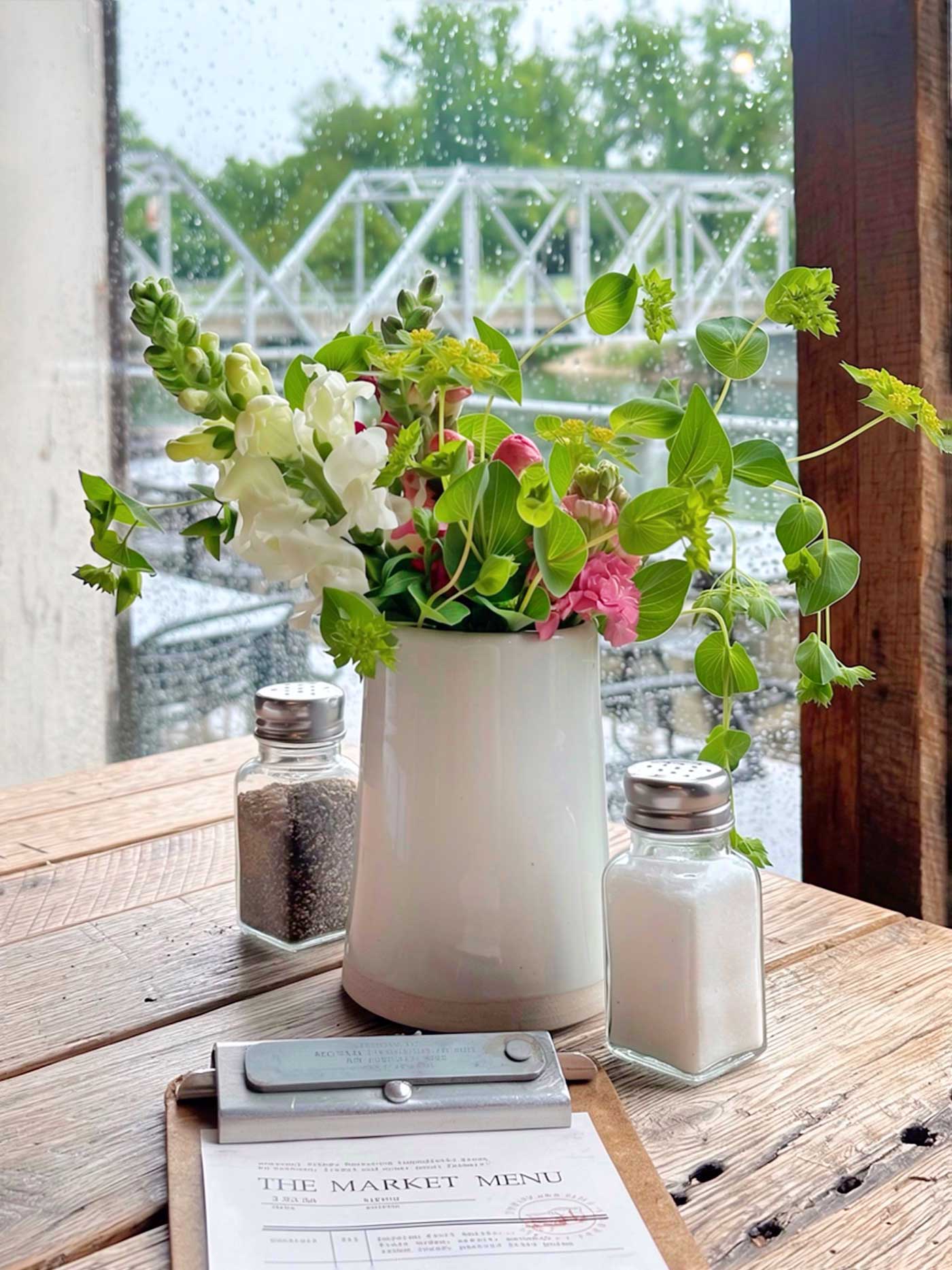 Fresh flowers in a vase on a restaurant table overlooking a river and bridge at The Ozark Mill in Missouri.