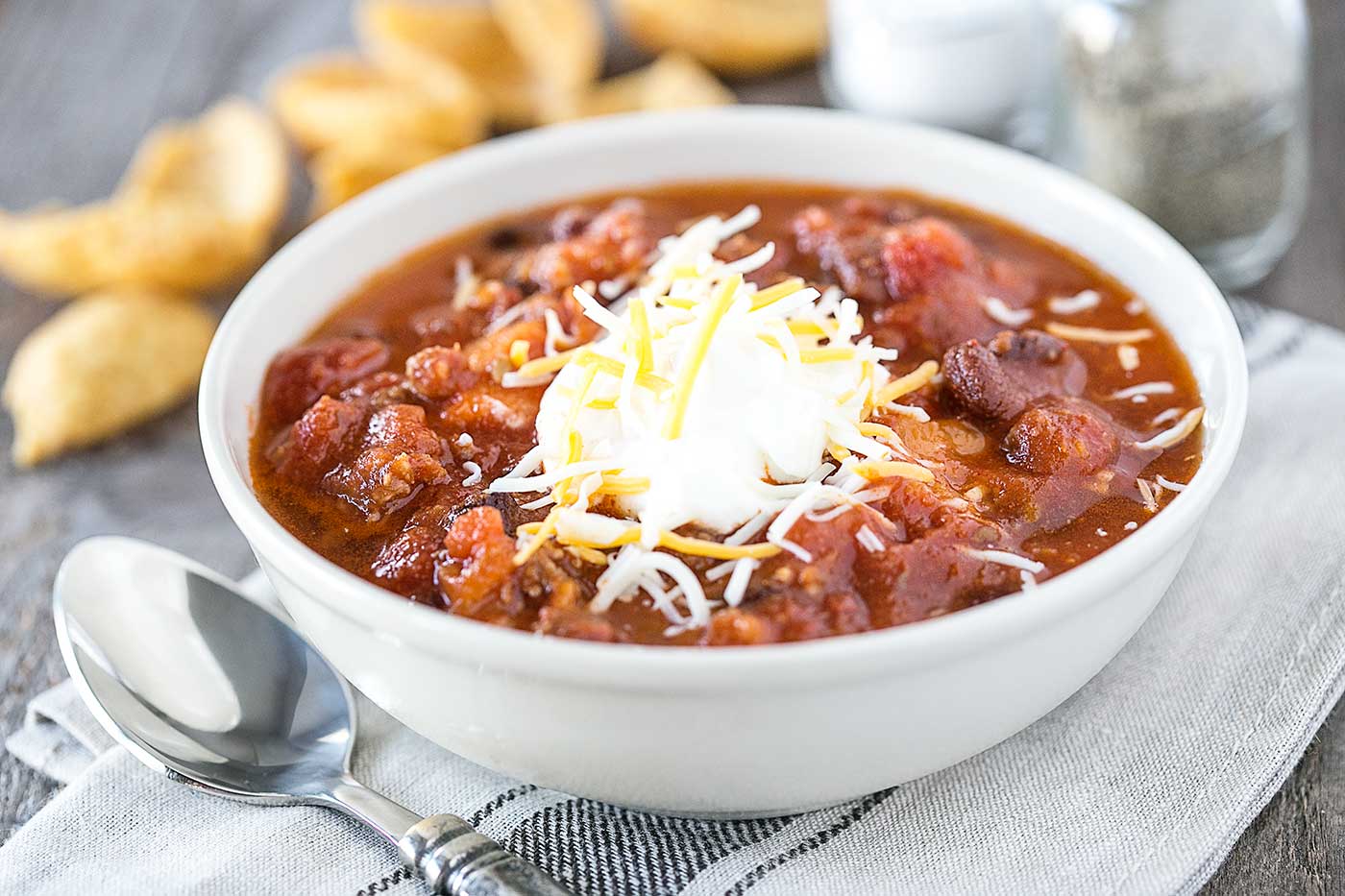 slow cooker sausage and sweet potato chili topped with shredded cheese and sour cream in a white bowl