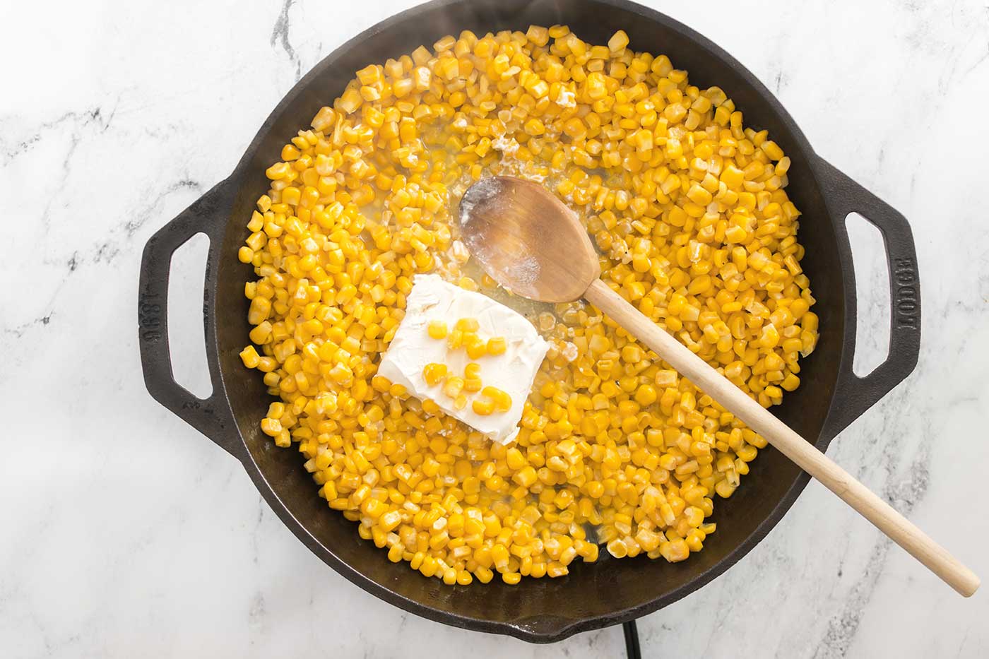 Cream cheese melting into sweet corn in a cast iron skillet