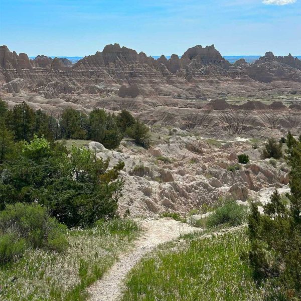 Square image of a narrow trail winding through the rugged terrain of Badlands National Park.