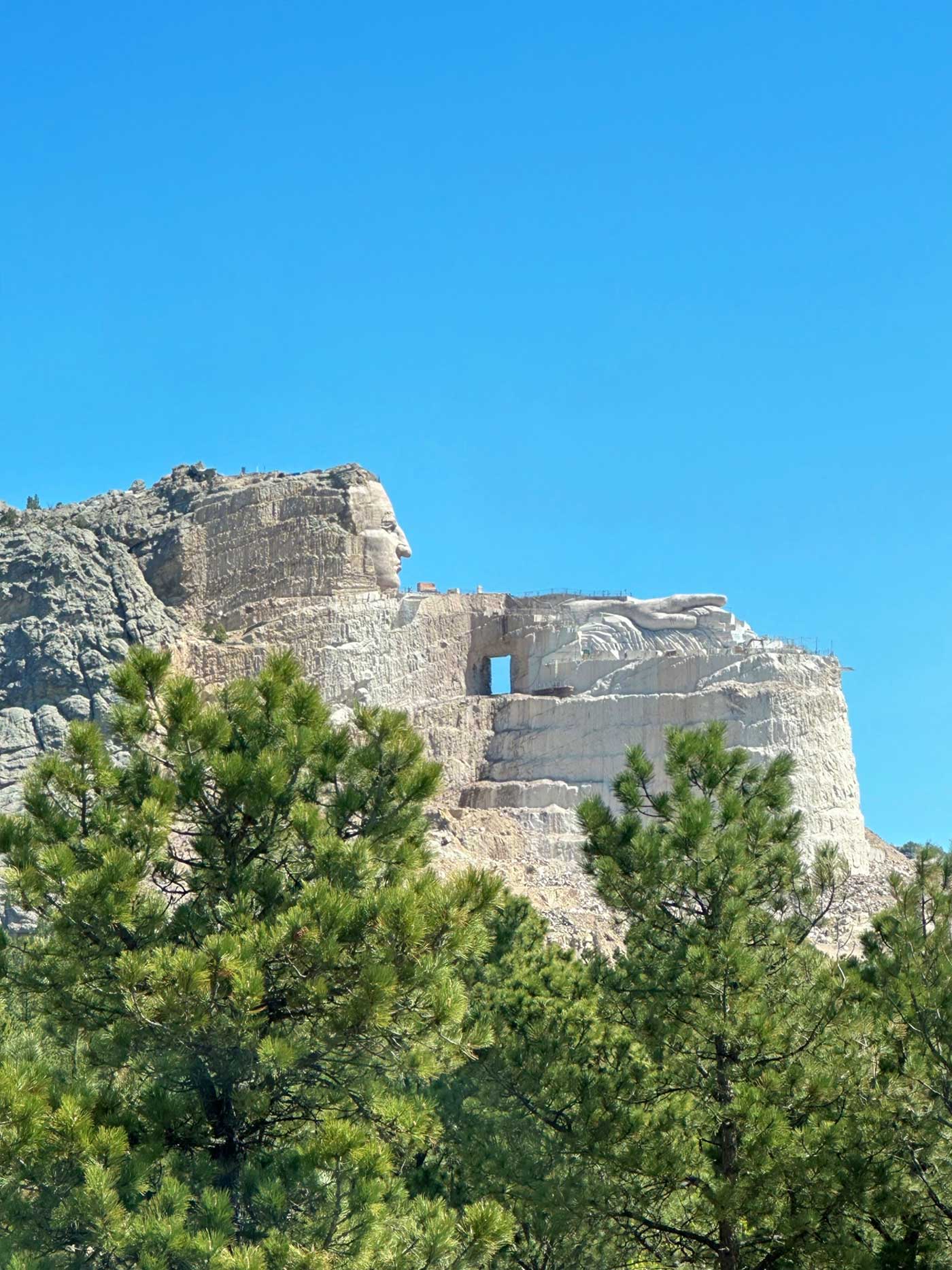 View of the Crazy Horse Memorial carving from a distance beneath a clear blue sky.