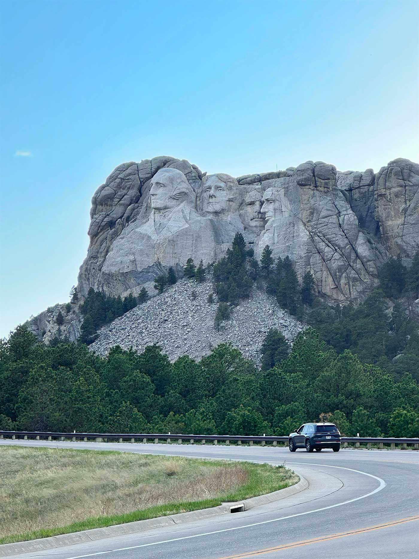 Mount Rushmore visible above the trees along a winding roadway in the Black Hills.