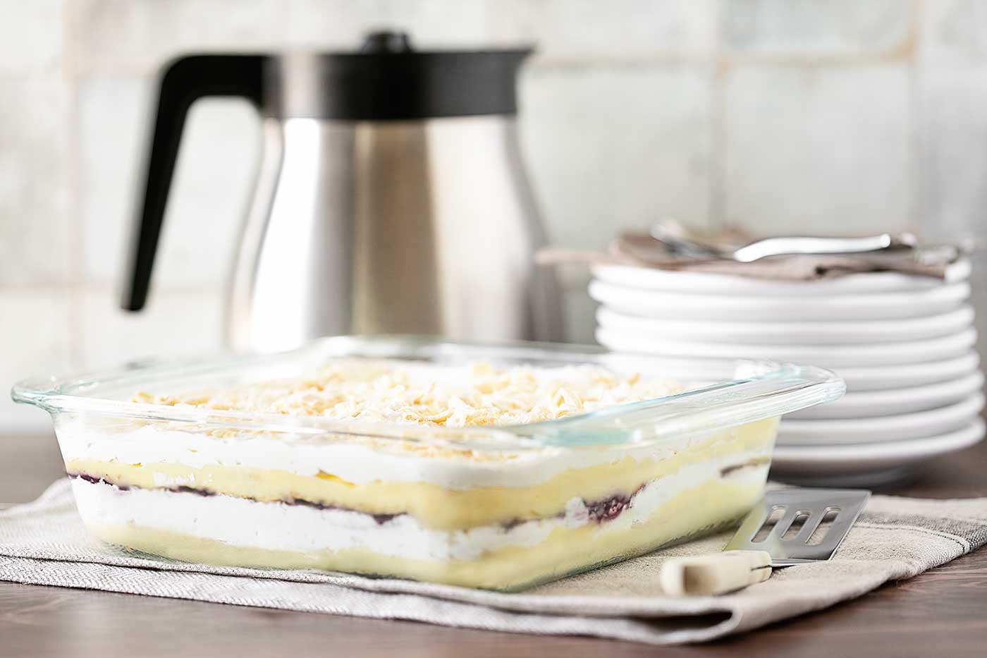 Flakie Saltine Cracker Dessert in a glass baking dish with visible layers of vanilla pudding, raspberry jam, whipped topping, and softened crackers.