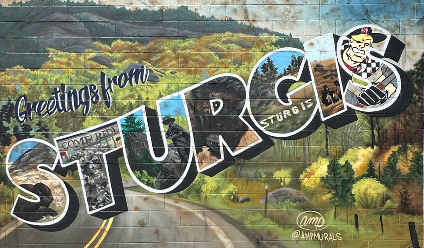 Colorful postcard-style Sturgis sign featuring scenic illustrations and local landmarks.