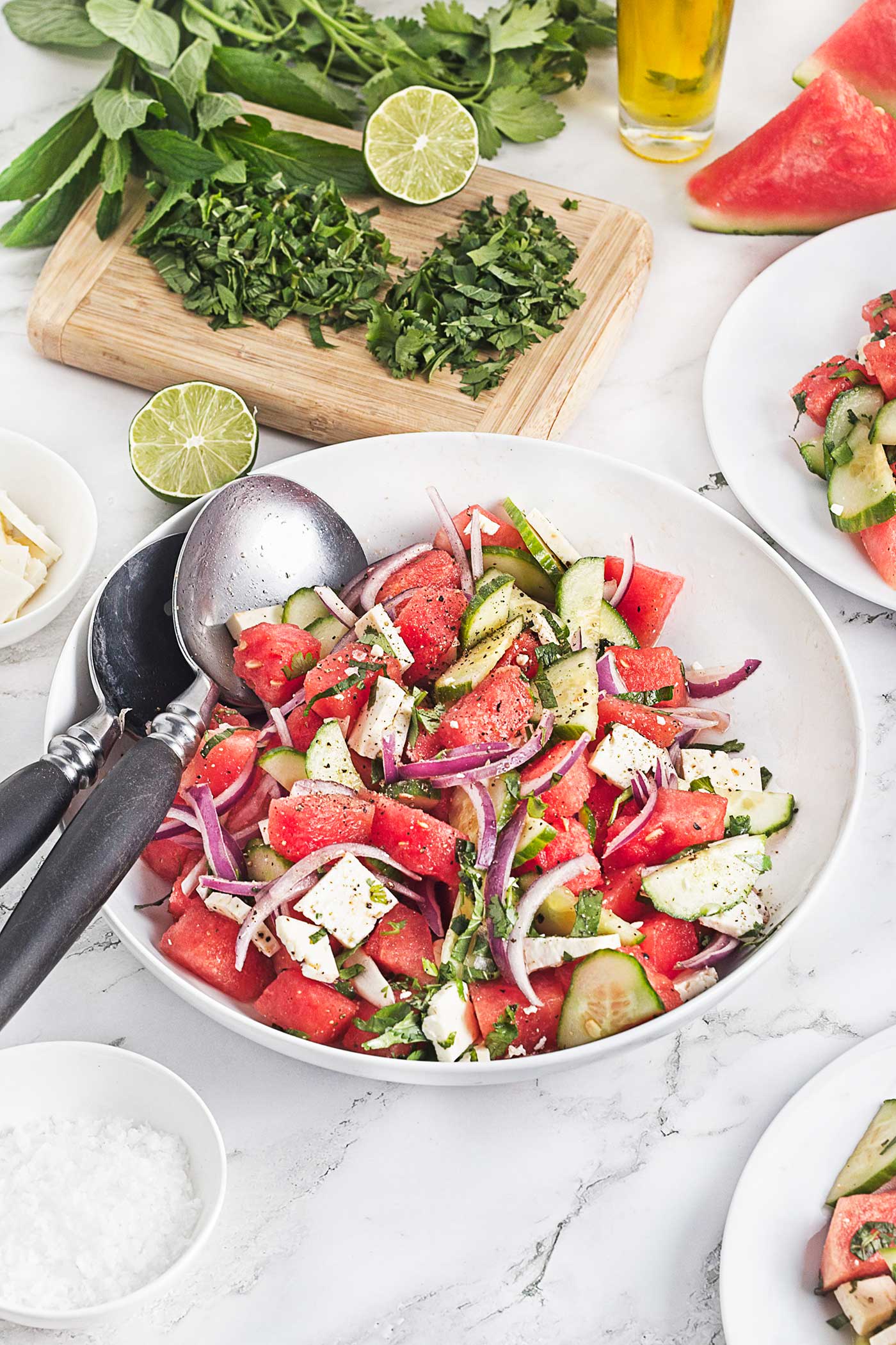 Watermelon feta salad with cucumber, red onion, herbs, lime, and olive oil arranged on a marble surface.