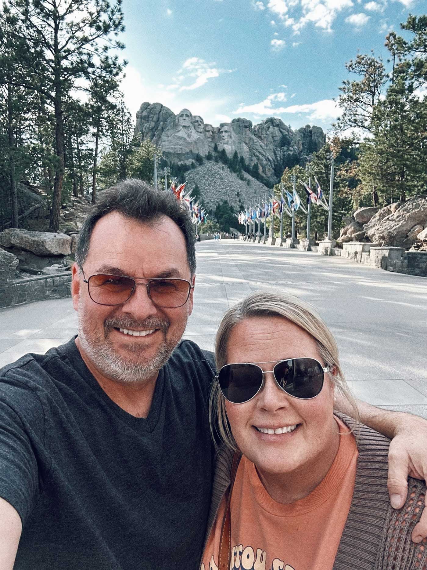 Couple smiling for a photo with Mount Rushmore visible in the background.