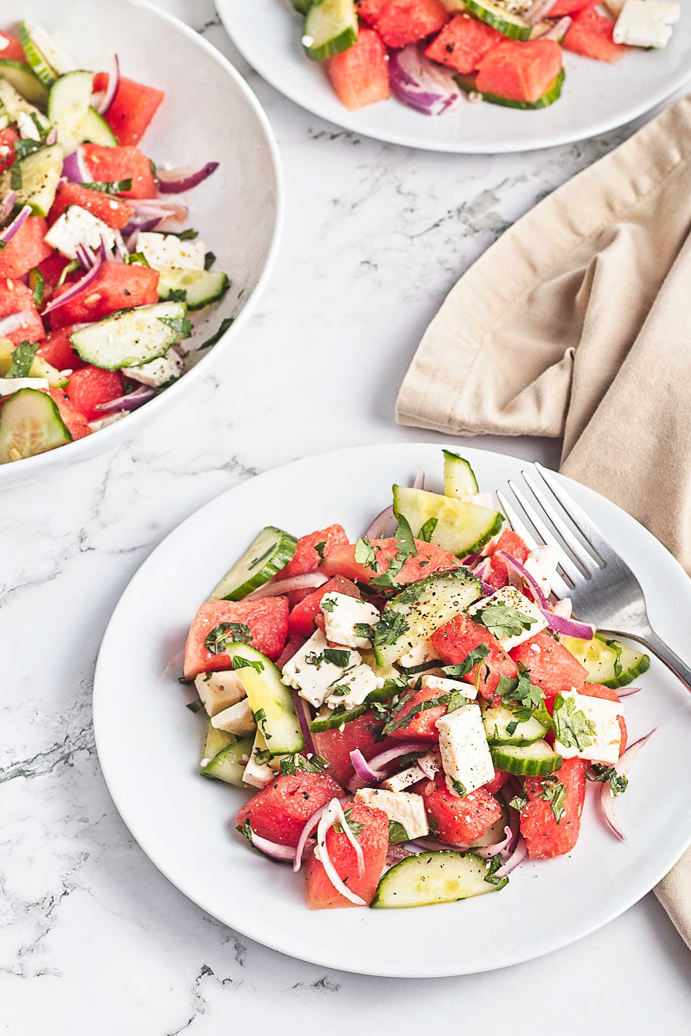 Watermelon feta salad with sliced cucumber, red onion, fresh herbs, and feta served on a white plate.