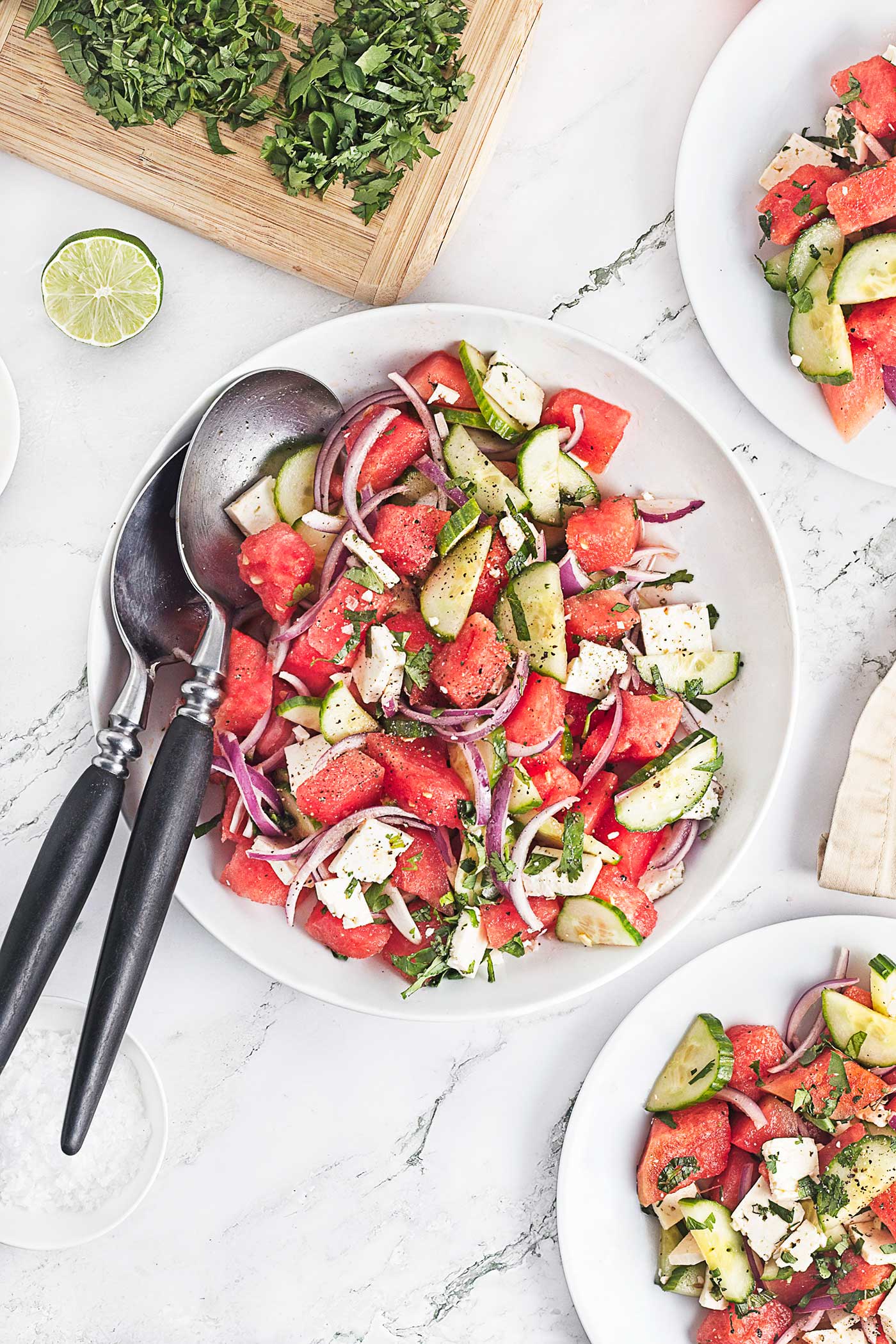 Overhead view of salad with fruit, vegetables and herbs served in a white bowl.