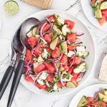 Close-up overhead photo of watermelon feta salad with cucumber, red onion, mint, cilantro, and lime in a white serving bowl.