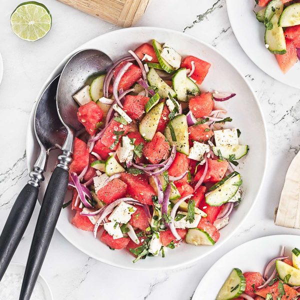 Close-up overhead photo of watermelon feta salad with cucumber, red onion, mint, cilantro, and lime in a white serving bowl.
