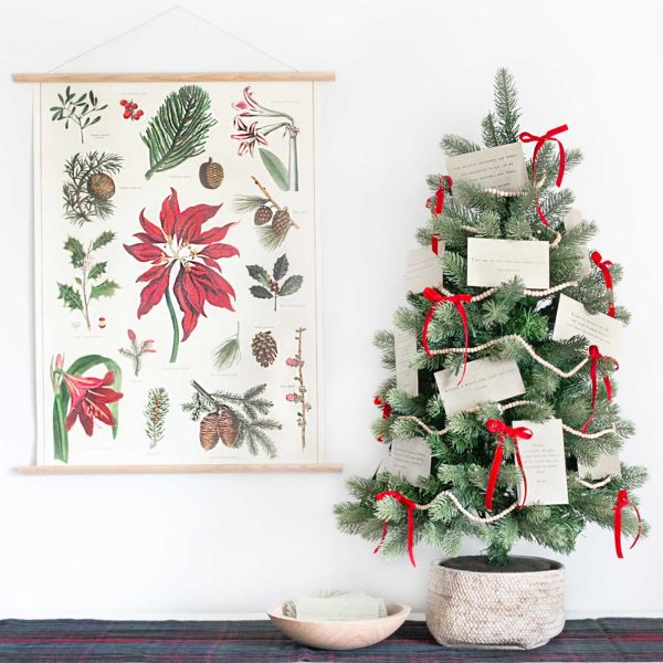 A tabletop Christmas Quote Tree decorated with vintage-inspired quote cards, red velvet ribbon, and wooden bead garland displayed beside a botanical Christmas print.