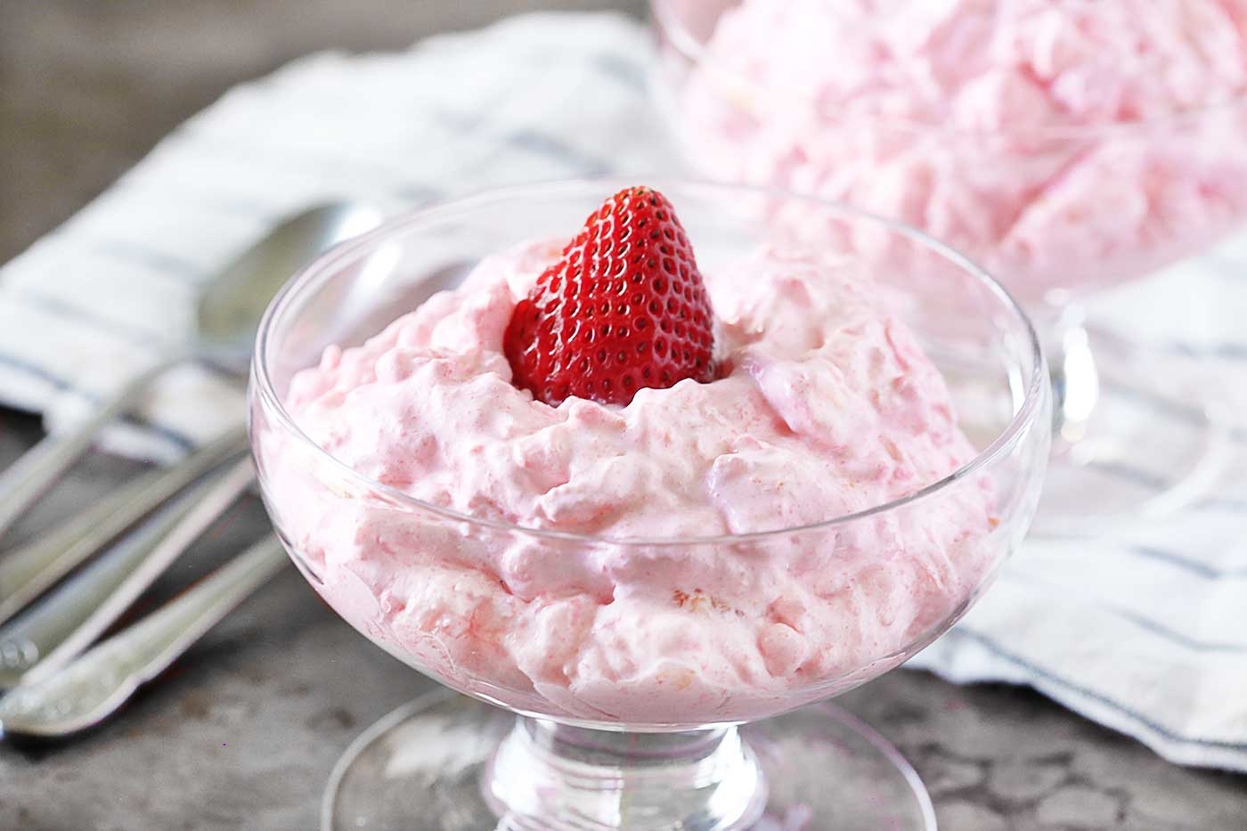 Pink cottage cheese Jello salad topped with a fresh strawberry and served in a clear dessert bowl.